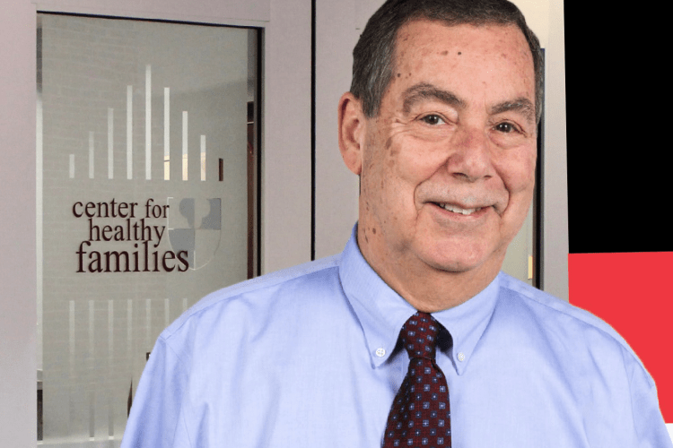 Dr Norm Epstein in shirt and tie smiles to camera with a smile and a twinkle in his eye