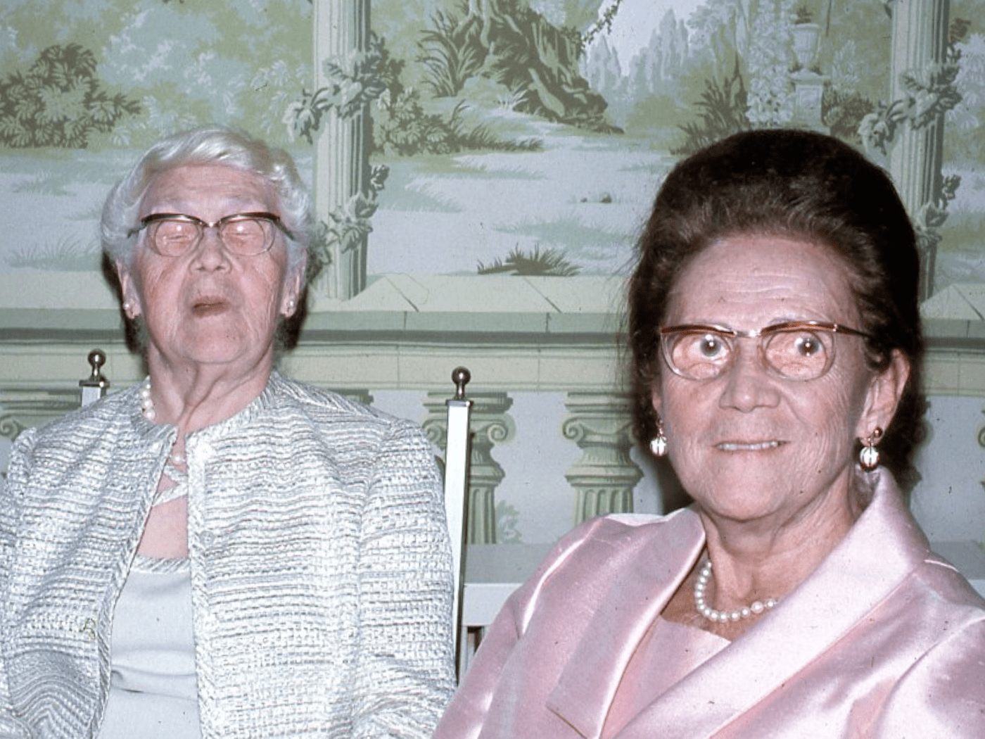 Two elder white ladies dressed nicely look at camera