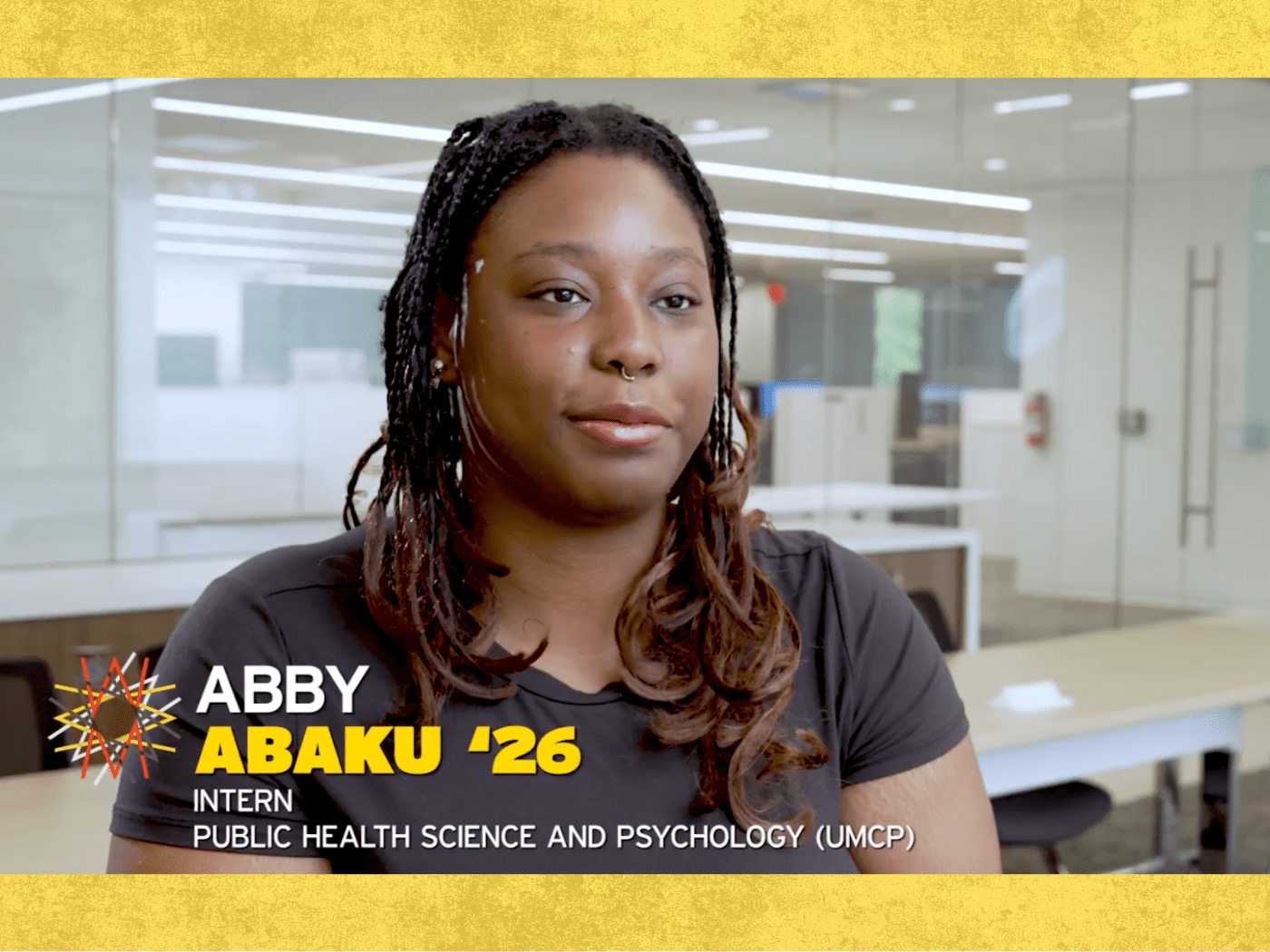 Black female student with long hair and black tshirt looks at camera, with her name on the bottom of the screen