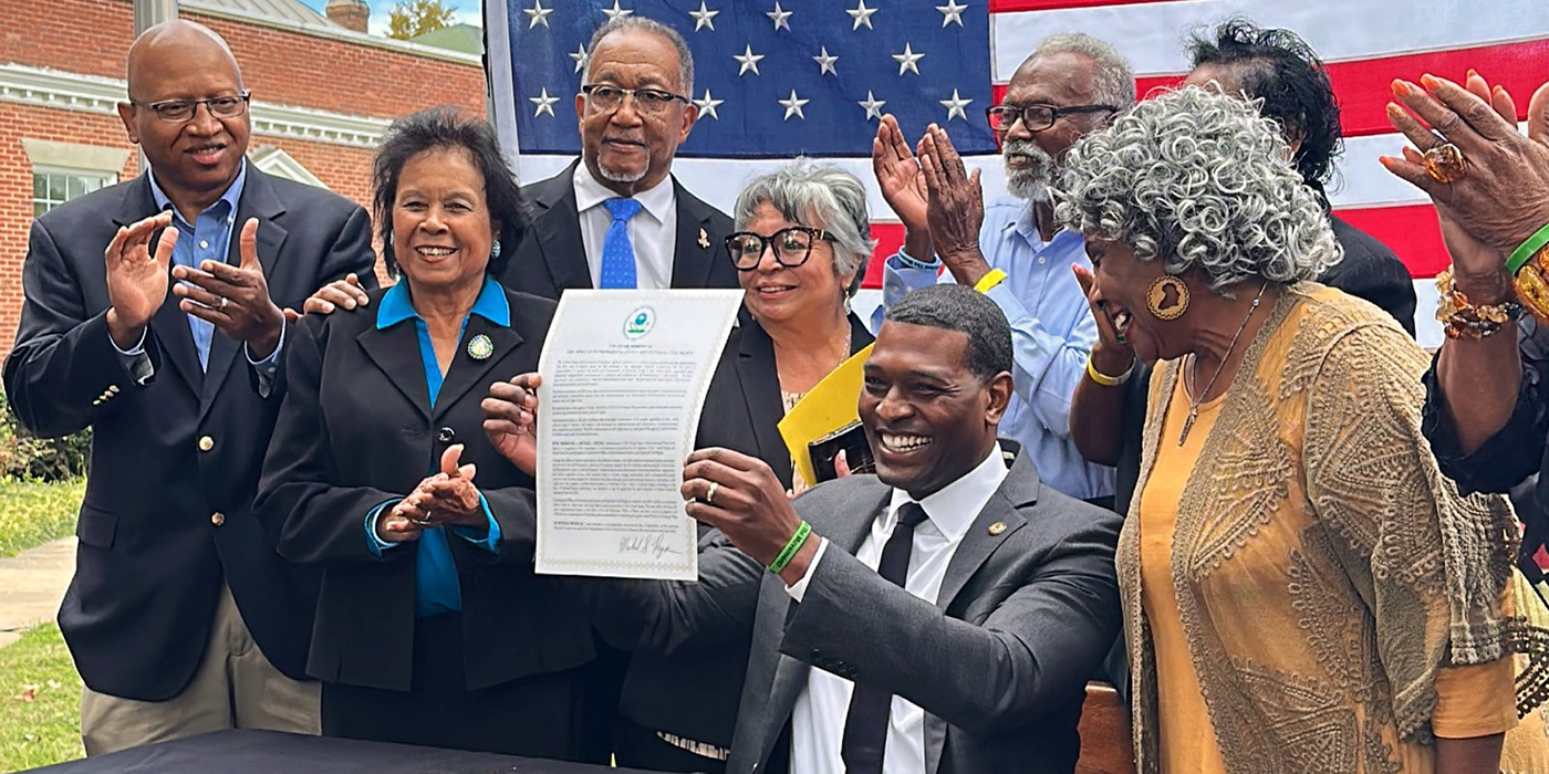 Group of happy African American environmental justice leaders stand in front of American flag, applauding announcement of new EPA office.