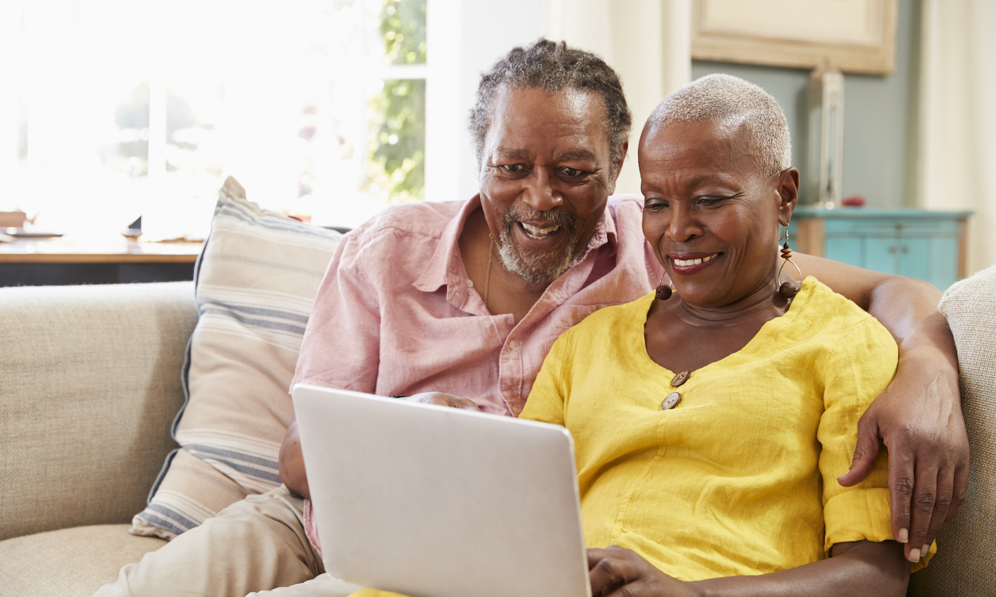 Attractive older African American couple smiling while looking at laptop computer while sitting on couch