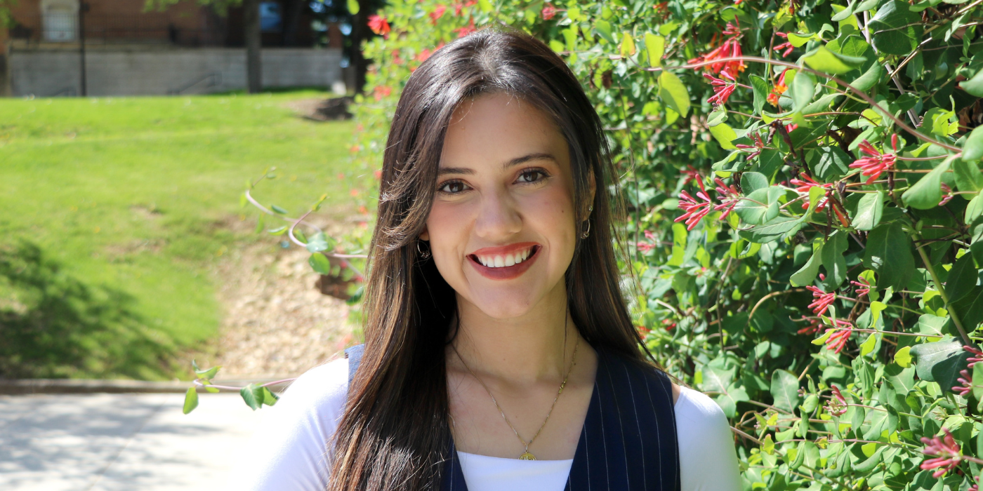 student graduation speaker smiles to camera, outside in front of flowers and grass