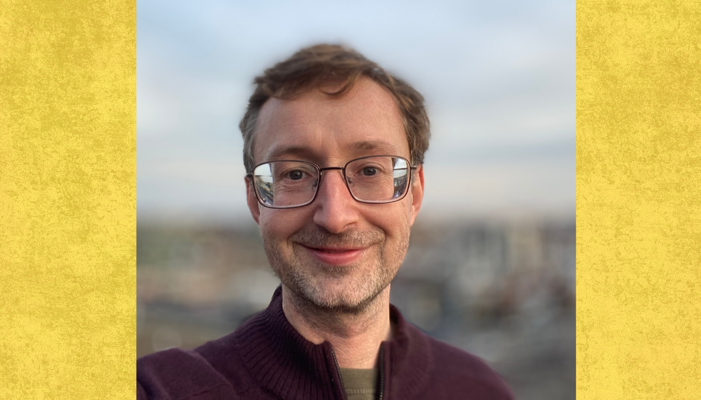 Professor smiles to camera with blurry cityscape behind him 