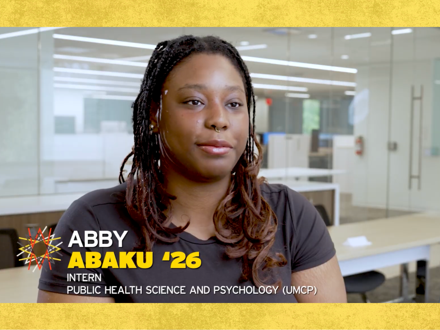 Black female student with long hair and black tshirt looks at camera, with her name on the bottom of the screen