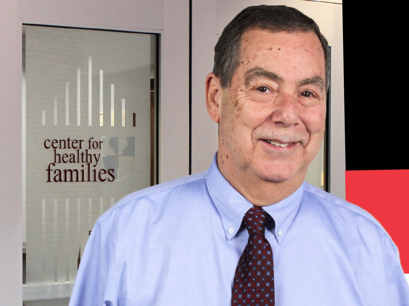 Dr Norm Epstein in shirt and tie smiles to camera with a smile and a twinkle in his eye