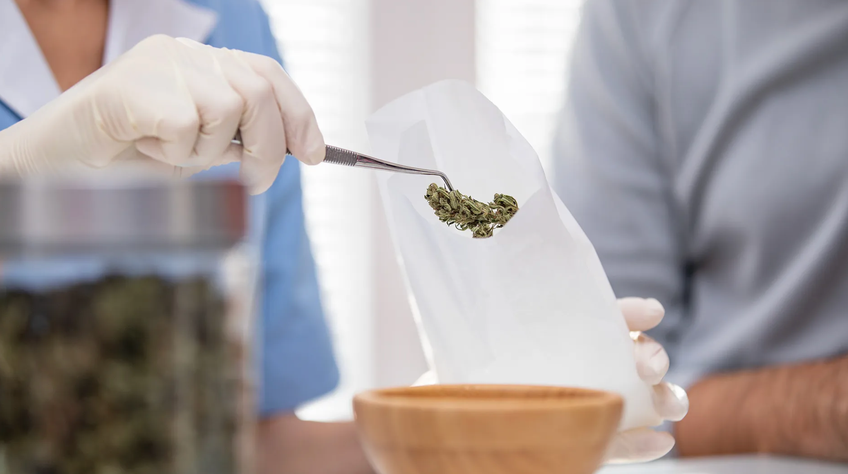 A white gloved hand holds a bud of marijuana with tongs, placing it in a bag
