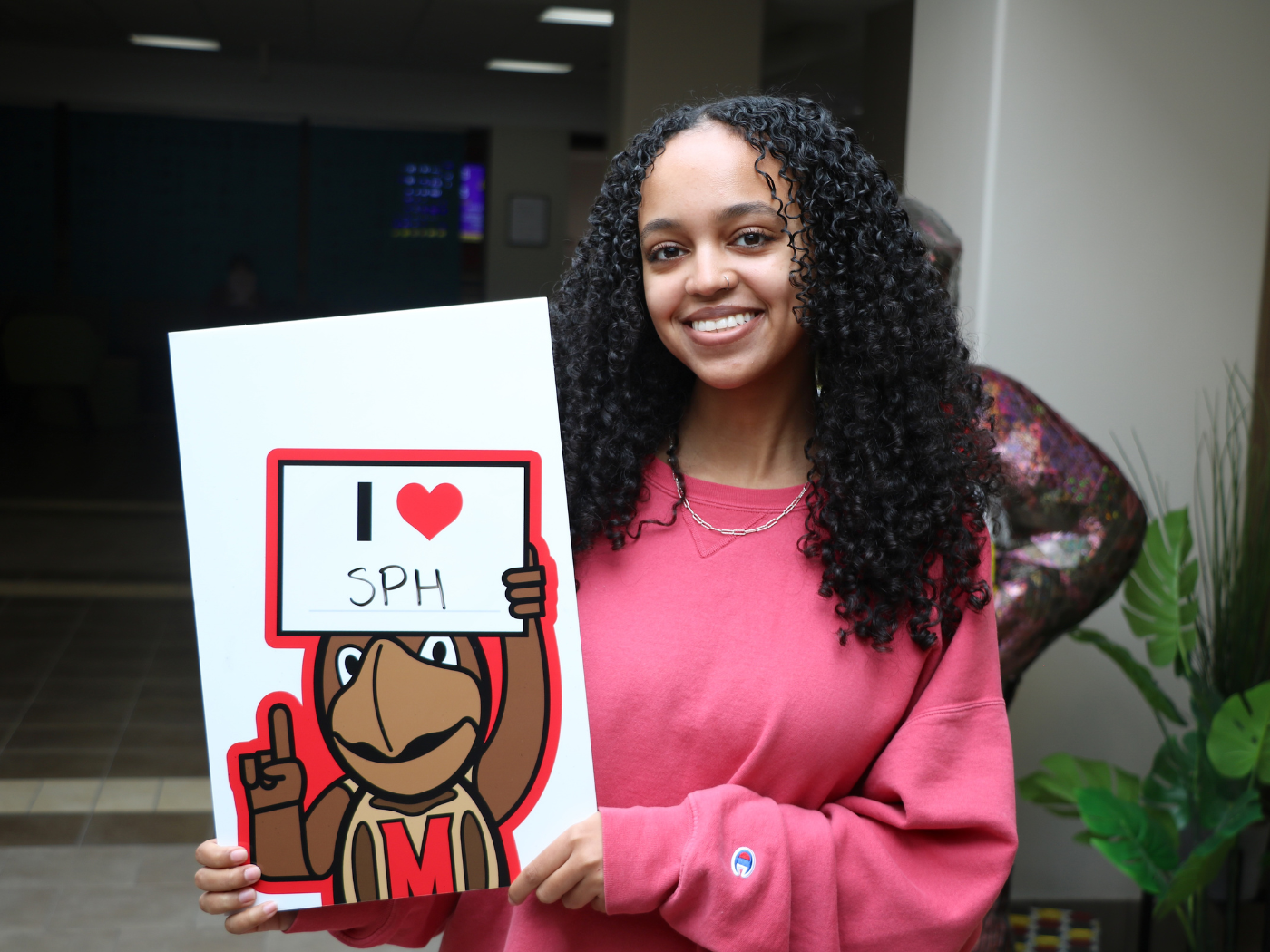 female student smiles to camera holding a sign that says I “heart” SPH