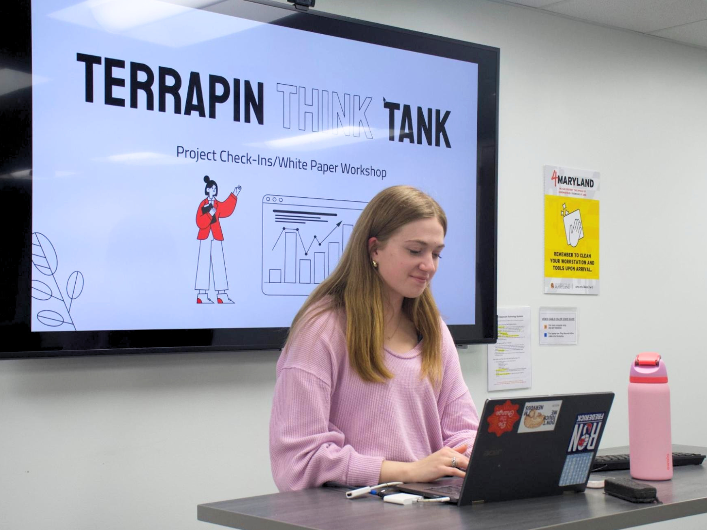 Student with blond hair works at laptop in front of big screen with words TERRAPIN THINK TANK