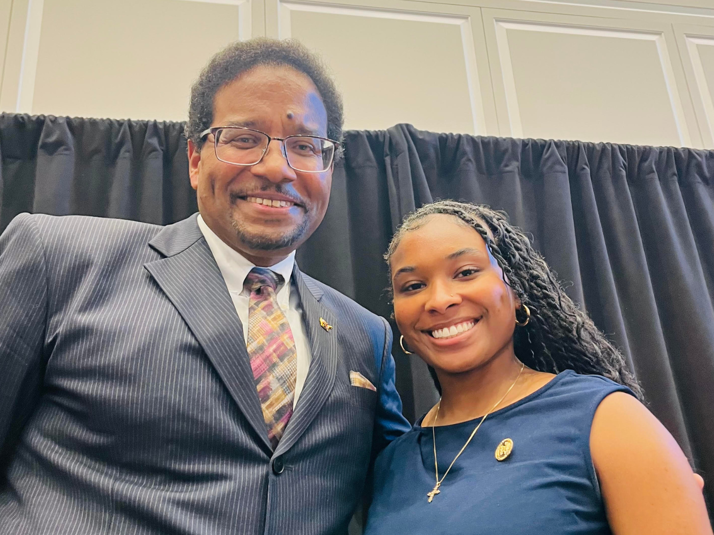 Black man in suit and young black student woman in teal top smile to camera