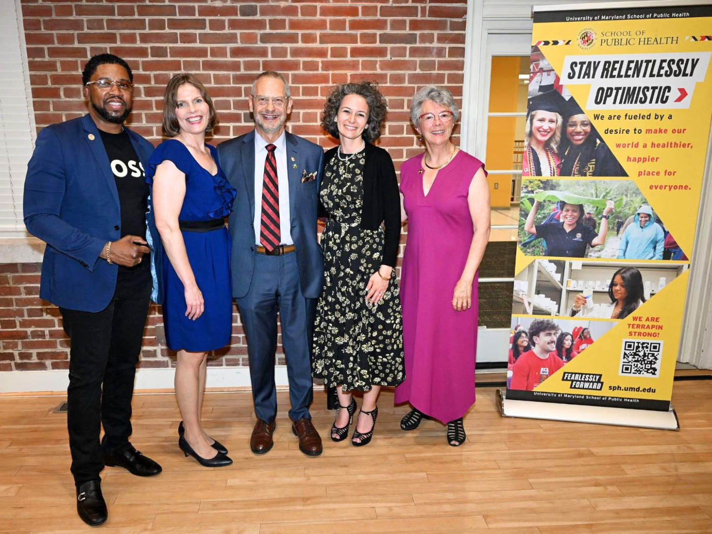 Group of 5 women and men dressed up and posing beside SPH banner