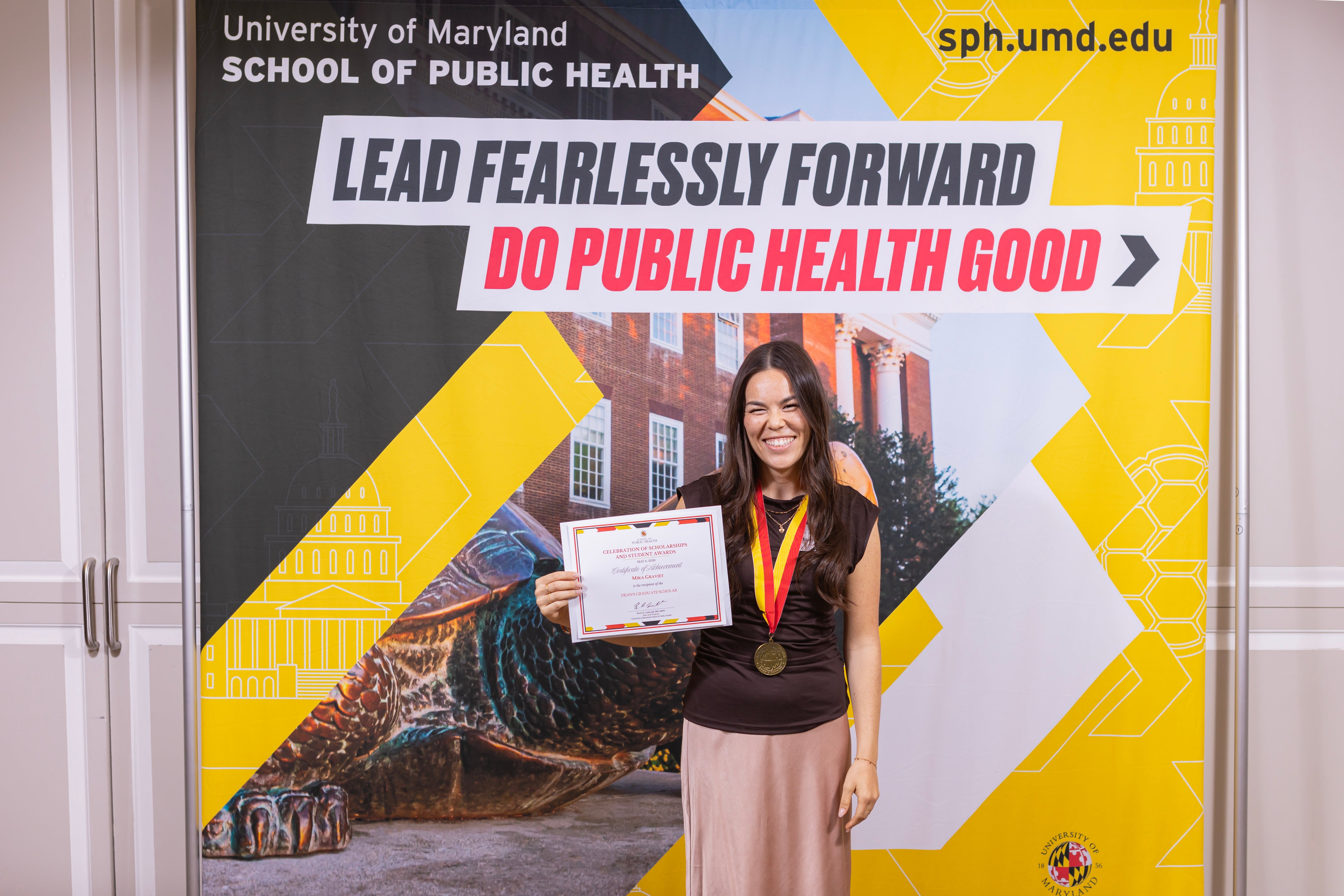 woman posing in front of a SPH backdrop with an award