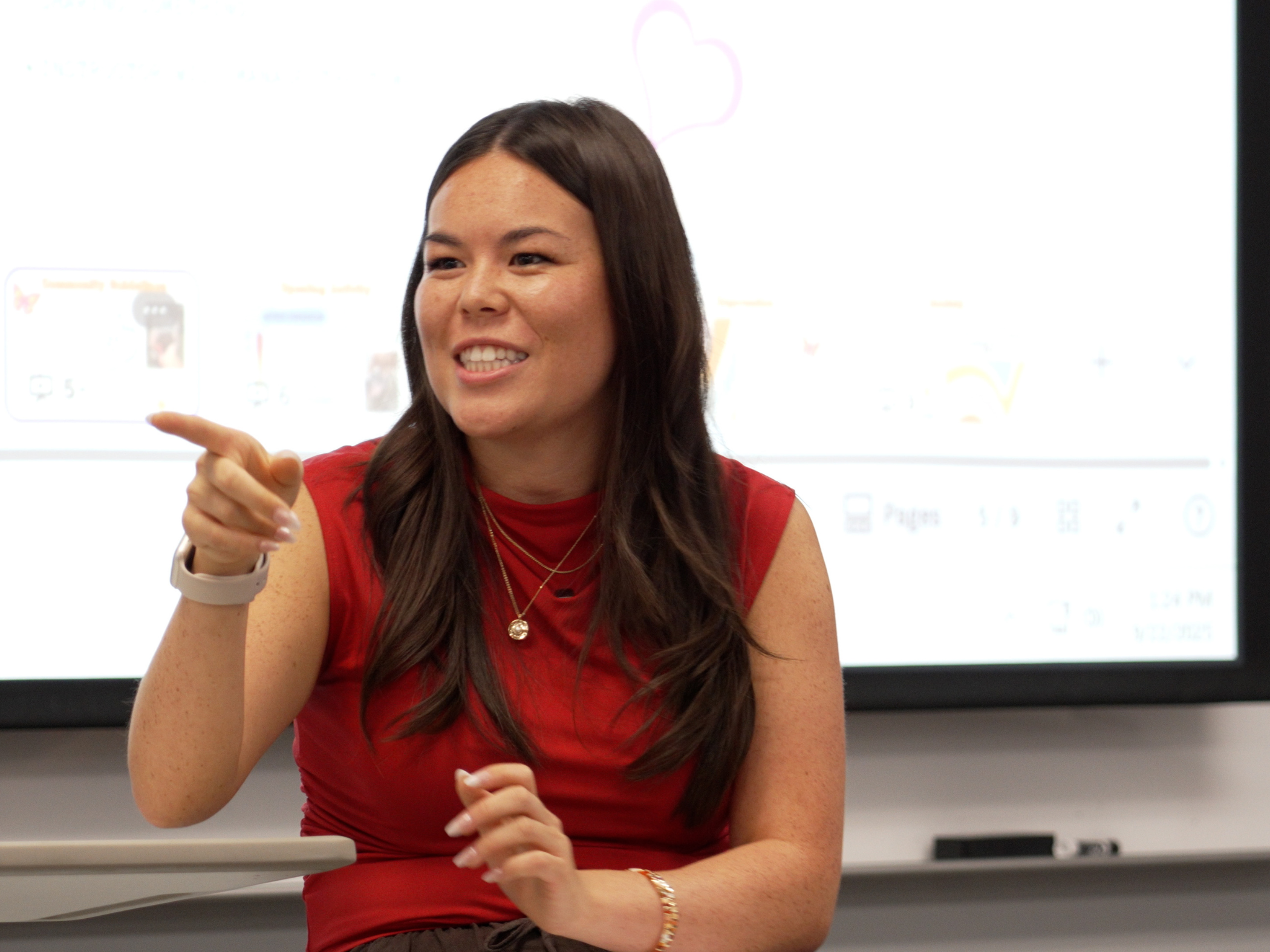 Woman with long brown hair and red sleeveless top instructing a class