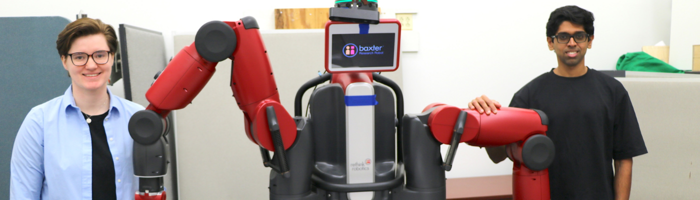 Two students posing on either side of a human sized robot