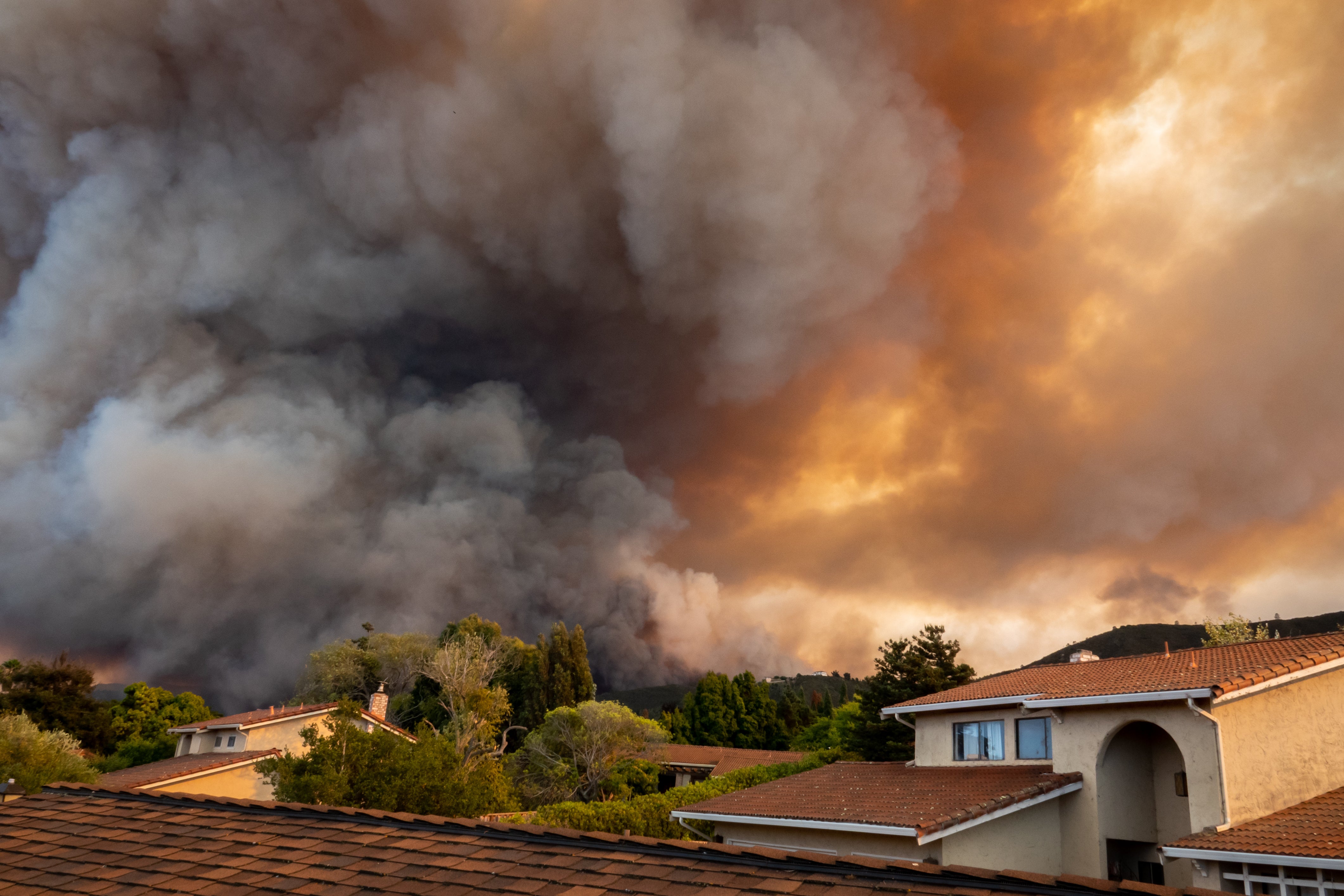 smoke billows in the sky with houses in foreground