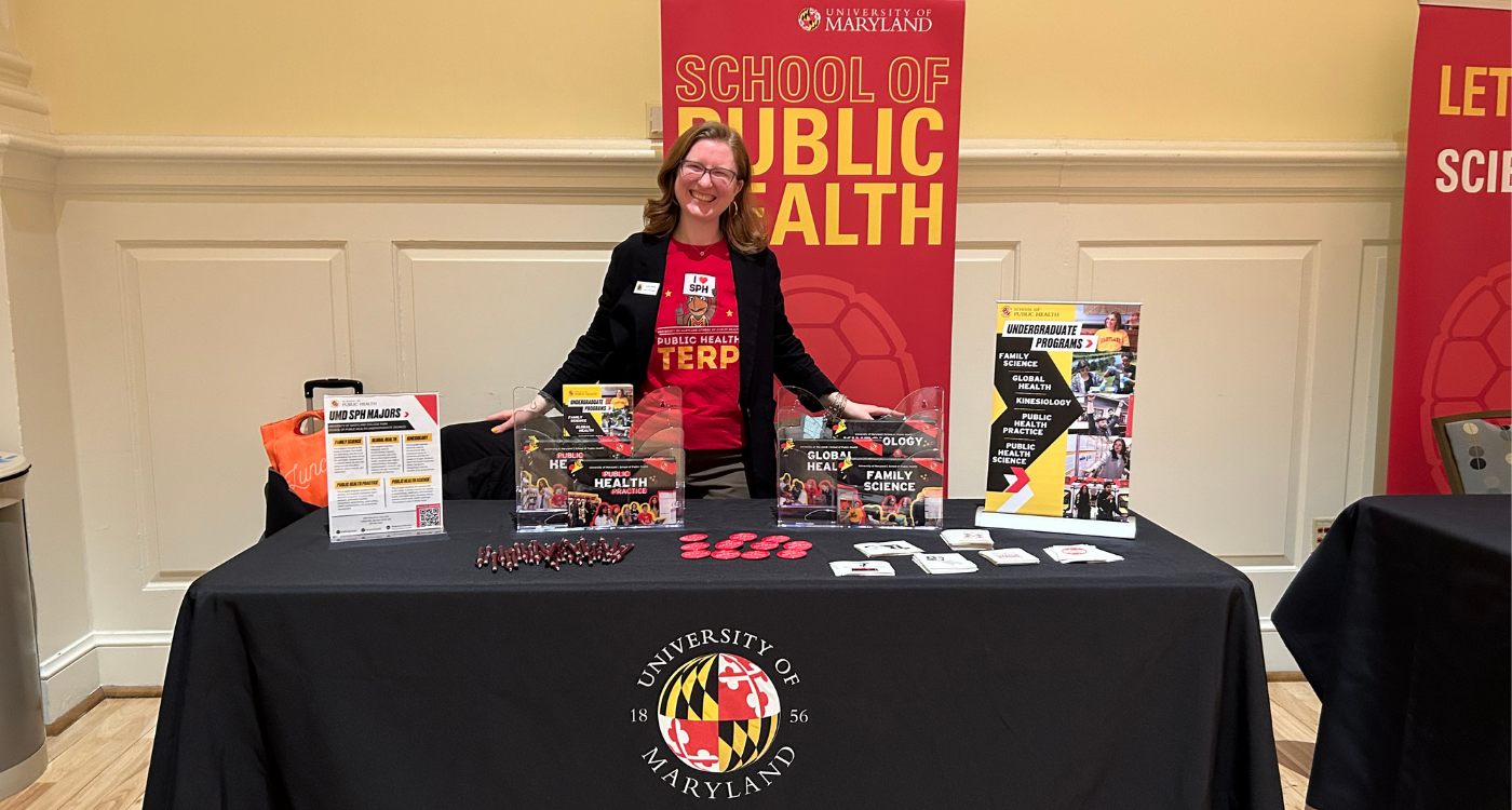 Woman smiles standing behind table full of promotional fliers for UMD school of public health
