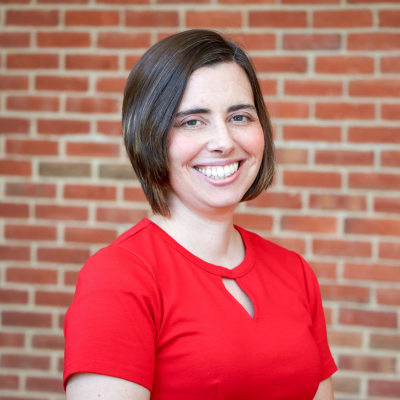 Caucasian woman with medium length brown hair wearing a red business attire top