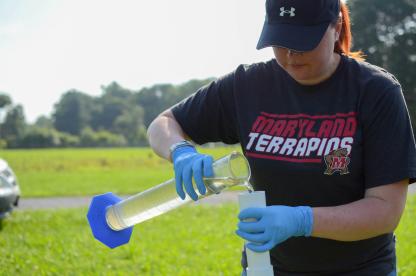 Student wearing gloves samples water for CONSERVE Center outdoors.