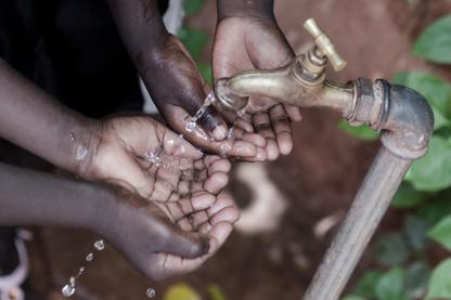 Two children in Ethiopia hold their hands under a running water spigot.