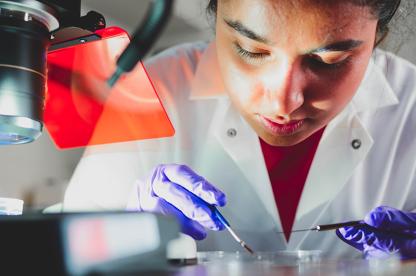 Student performing task in lab with petri dish and tools.