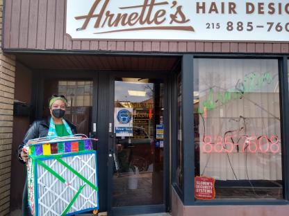 A Black woman holding a COVID-19 air filter in front of a hair salon