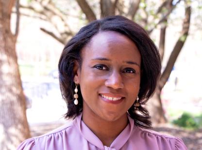 Outdoor headshot of a smiling person wearing a light blouse and drop earrings.