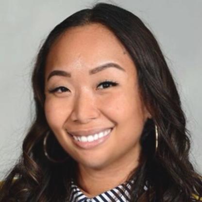 Headshot of a smiling person with long dark hair and hoop earrings against a neutral background.