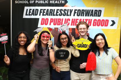 Group of students pose with School of Public Health props in front of a ‘Lead Fearlessly Forward’ backdrop.