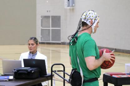 Student in scrubs holds a ball during a lab activity while an instructor records data.