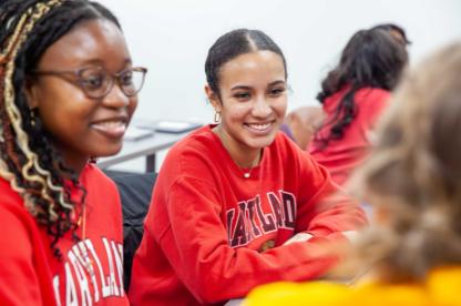 Two students in red Maryland sweatshirts sitting at a table and talking during a group activity.