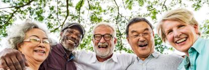 five elders with arms around each other smile to camera with tree canopy in background