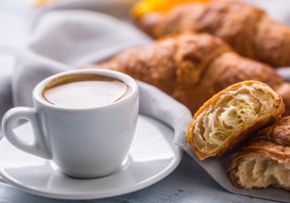 White cup of coffee on a saucer beside croissants, including one cut open.