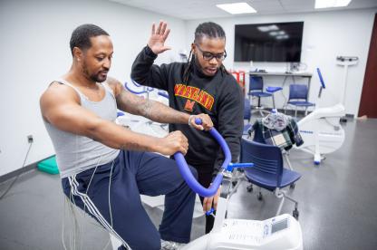 Man on exercise bike for a test and male student assists in study