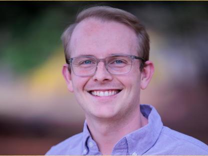 White man with wire rimmed glasses, short brown hair, lavender button-down smiling