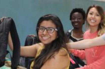 Three students smile together in a classroom or group activity setting.