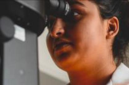 Student looks through a microscope in a laboratory setting.