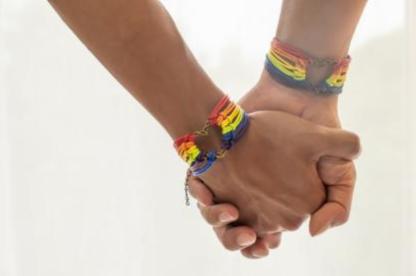 Two brown arms with rainbow bracelets hold hands 