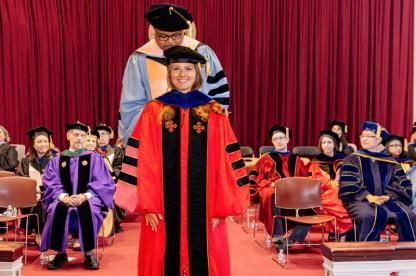 Woman getting her doctoral hood put on by a faculty member