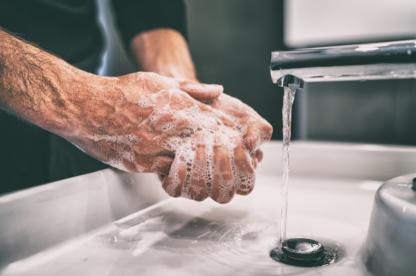 Close-up of a person washing their hands with soap under running water in a sink, illustrating proper hand hygiene.