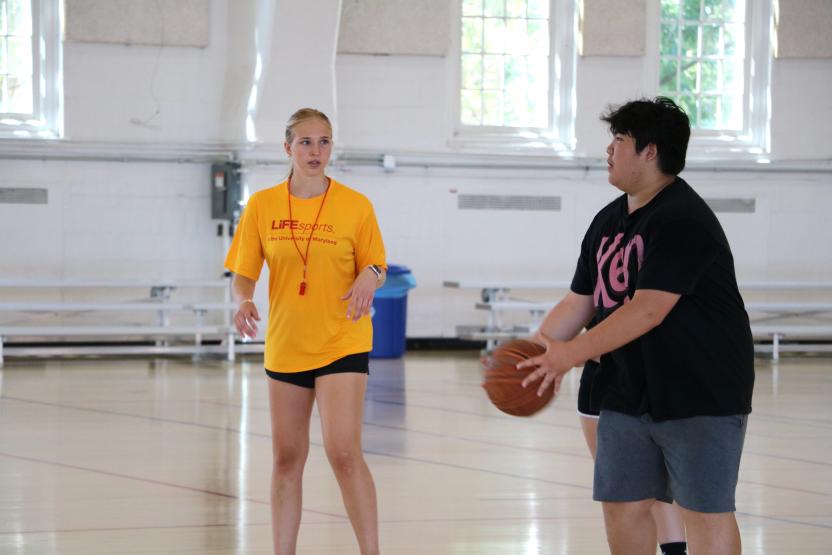 Counselor coaching a kid in shooting a basketball