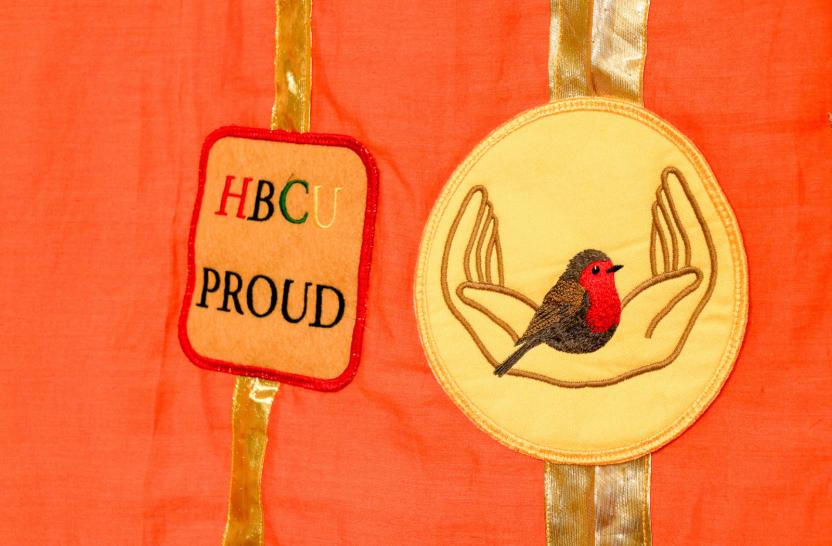 Detail of quilt, orange fabric with two symbols sown on to gold ribbon. 