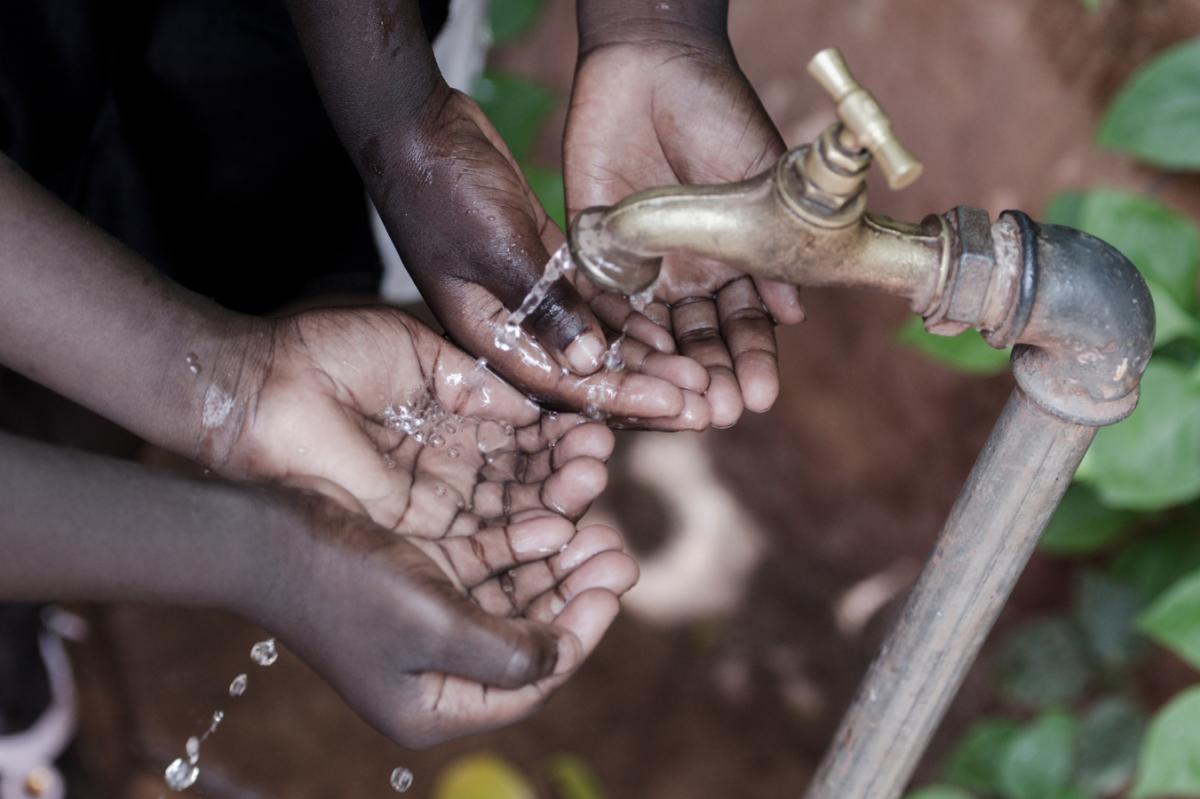 Two children in Ethiopia hold their hands under a running water spigot.