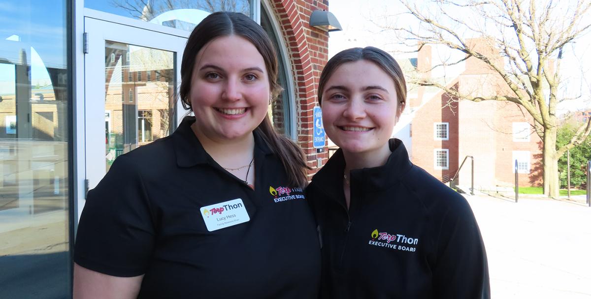 Two young women stand next to each other outside, wearing black shirts.