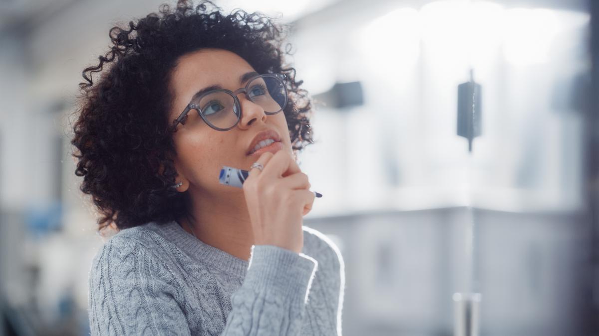 Woman with curly hair and glasses in a classroom looking up at something
