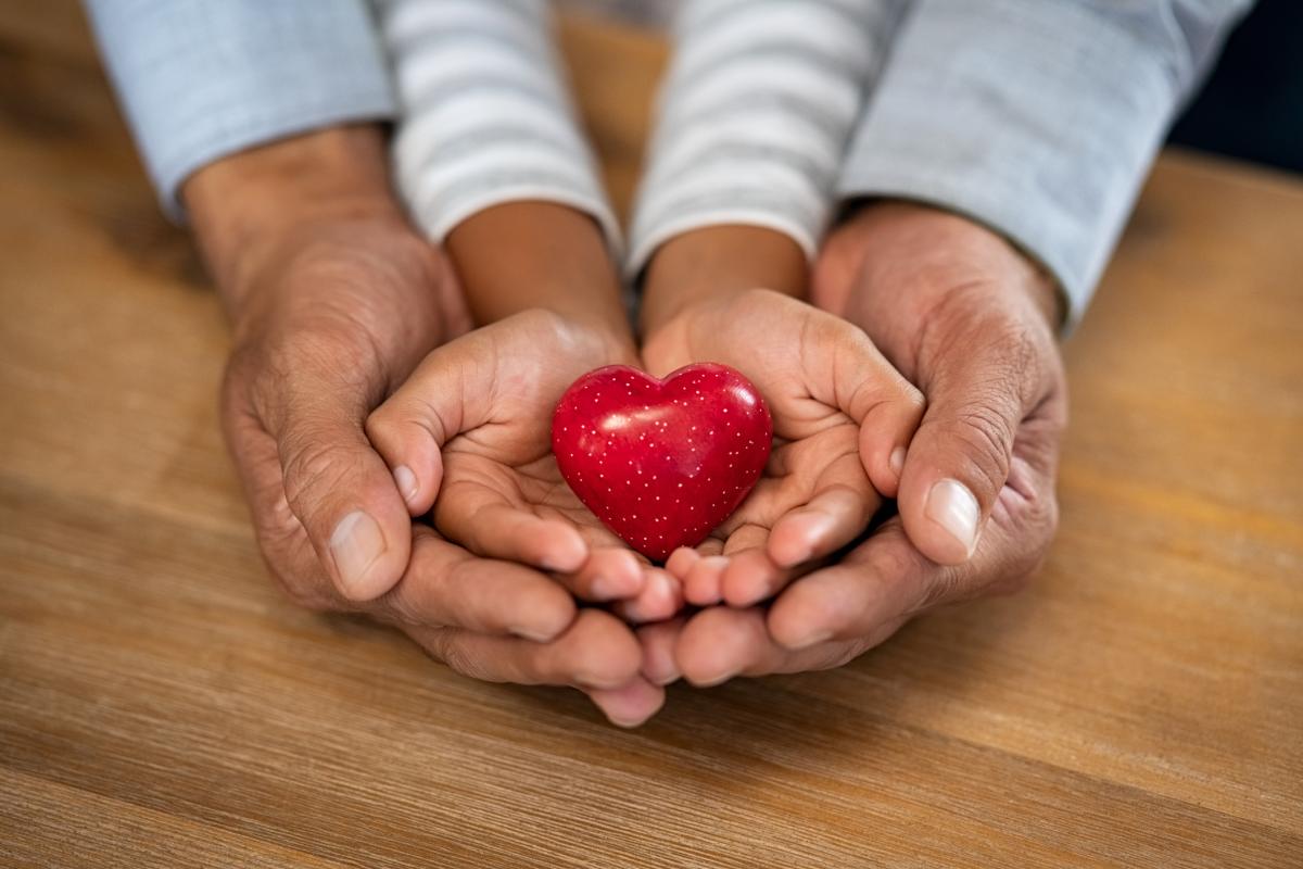 Family holding small red heart in hands on wooden background.