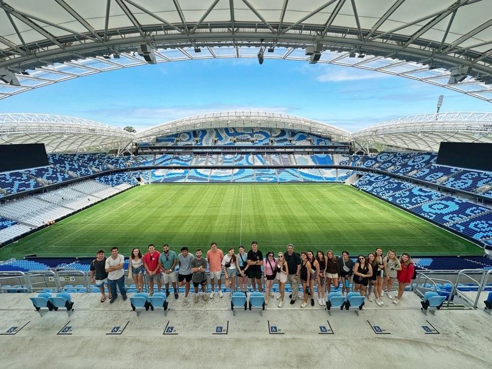 Row of students with green field behind them inside of a stadium.