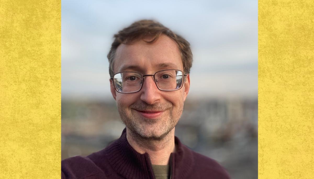 Professor smiles to camera with blurry cityscape behind him 