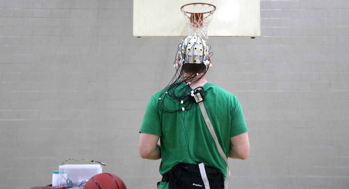 Man with wired brainwave cap on standing at a basketball free throw line