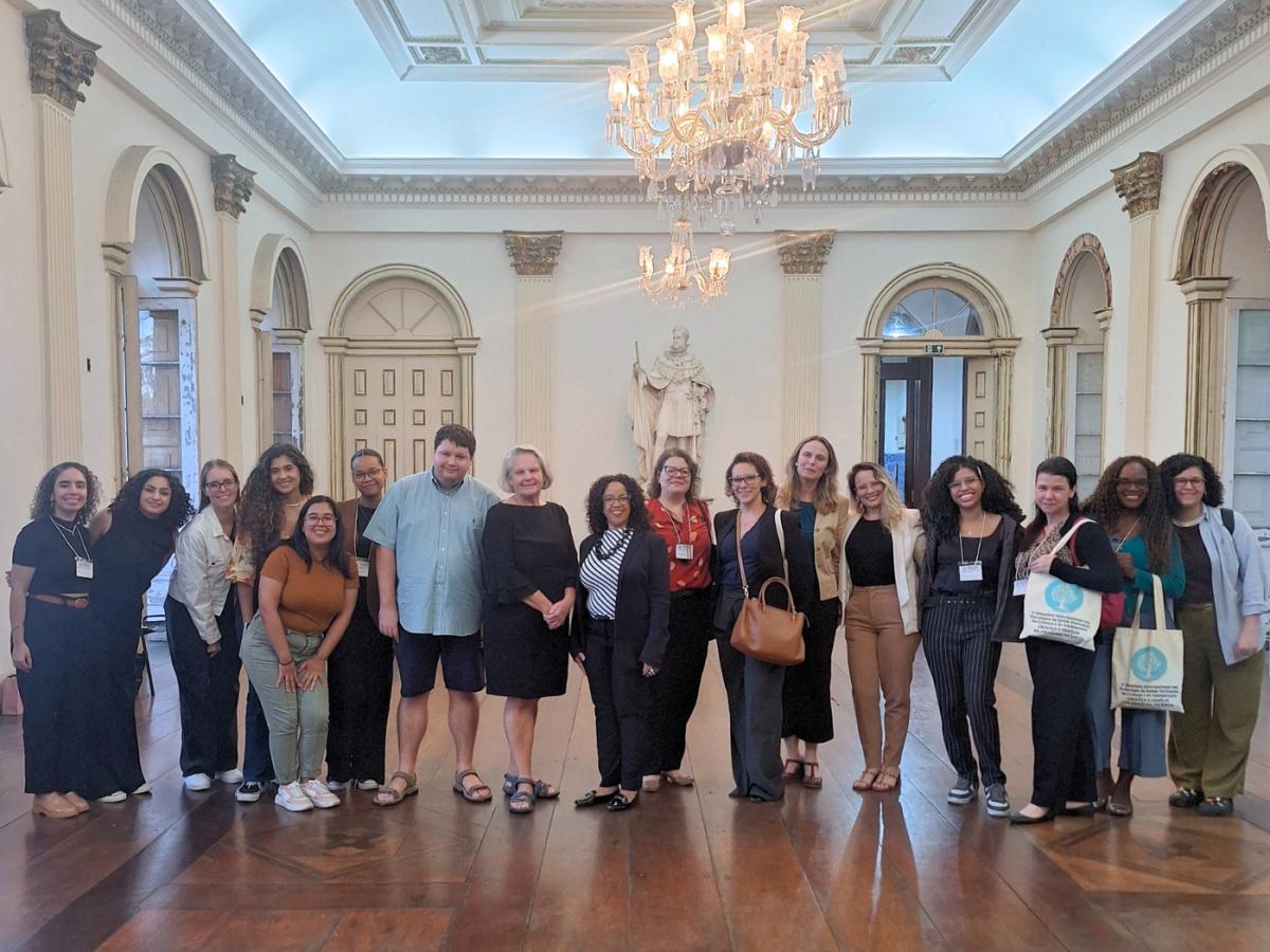 Group of students and faculty pose in a grand high ceilinged room with a chandelier.