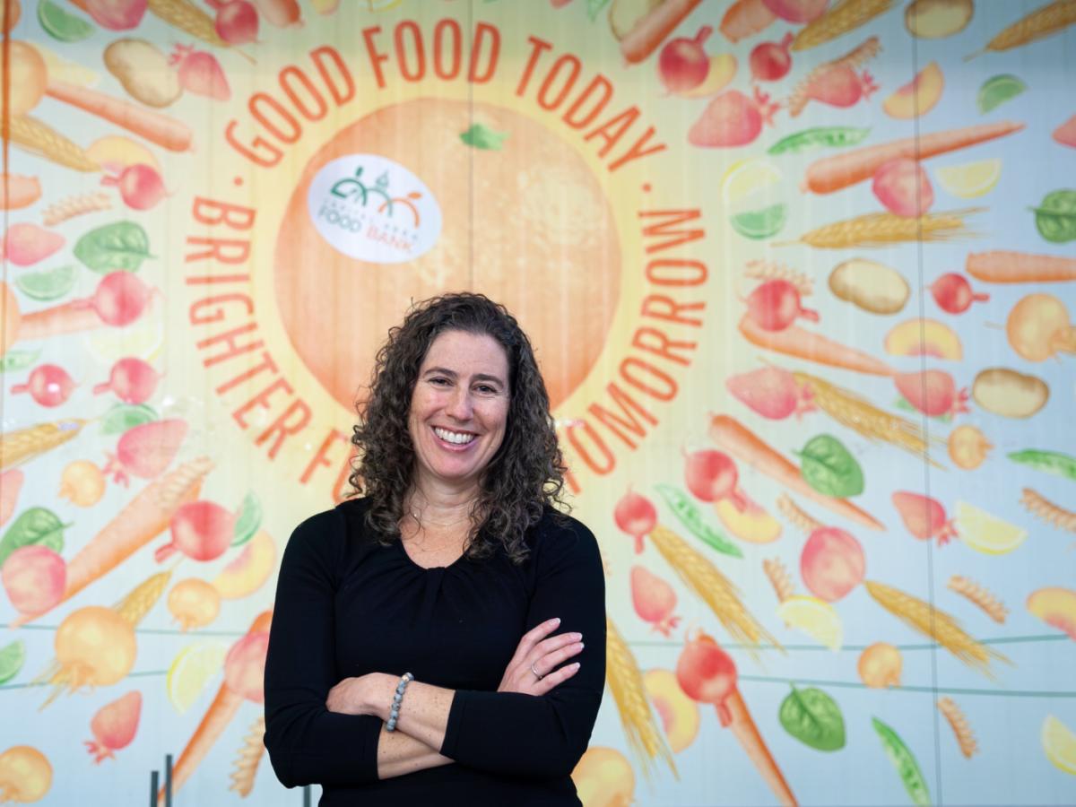 Woman with curly long hair in a black top smiles in front of a wall mural.