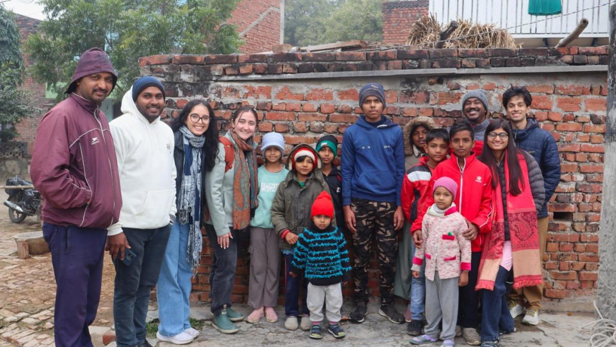 Group of communities members in Varanasi stand with two UMD students in front of a brick building
